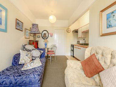 A living area with a blue patterned sofa, cream armchair, table with two chairs, and a kitchenette at Clooneavin Apartment 5 in Lynmouth near Lynton