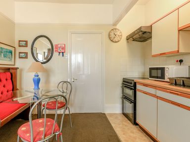 A kitchen with a glass table, red cushioned chairs, a blue lamp, a stove, microwave, and cabinets at Clooneavin Apartment 5 in Lynmouth near Lynton