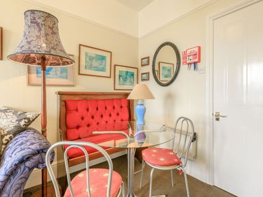 A small dining area with a glass table two chairs with red cushions a red upholstered bench a floor lamp and wall art at Clooneavin Apartment 5 in Lynmouth near Lynton