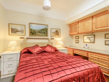 A bedroom with a red bedspread a double bed two bedside tables with lamps wooden cabinets and a wall sink at Clooneavin Apartment 5 Lynmouth near Lynton