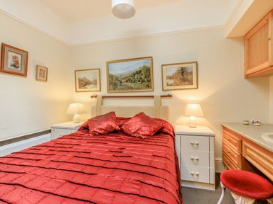 A bedroom with a red bedspread on the bed two bedside tables with lamps and framed paintings on the walls at Clooneavin Apartment 5 Lynmouth near Lynton