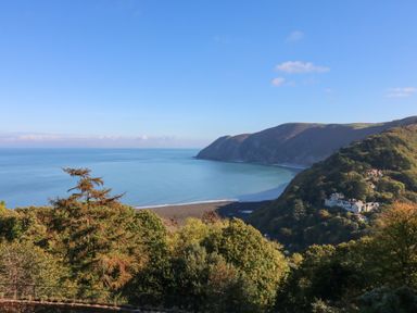 A coastal view with trees in the foreground a bay with calm water and hills in the background at Clooneavin Apartment 8 Lynmouth near Lynton