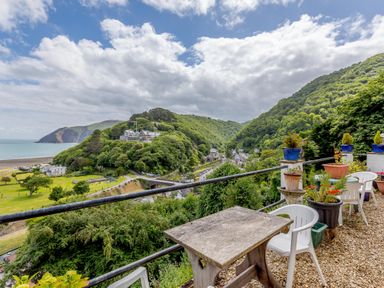 A terrace with plastic chairs and potted plants overlooking green hills and a coastal village at Clooneavin Apartment 8 Lynmouth near Lynton
