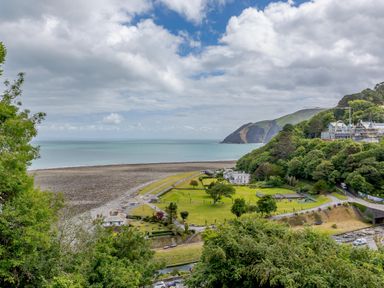 A coastal landscape with green fields trees a pebble beach and hills in the background at Clooneavin Apartment 8 Lynmouth near Lynton