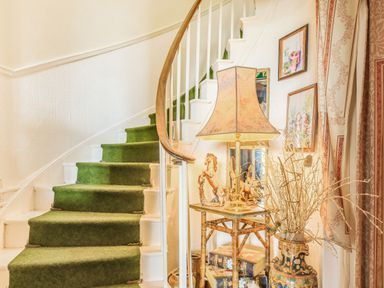 A curved staircase with green carpet and white railing next to a small table with a lamp horse figurine and decorative vase at Clooneavin Apartment 8 in Lynmouth near Lynton