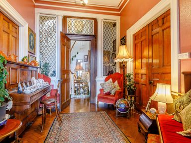 A sitting room with wooden doors piano chairs armchairs lamps and decorative plates at Clooneavin Apartment 8 in Lynmouth near Lynton