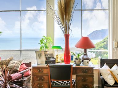 A room with a wooden desk and chair in front of a large window showing a sea view at Clooneavin Apartment 8 in Lynmouth near Lynton