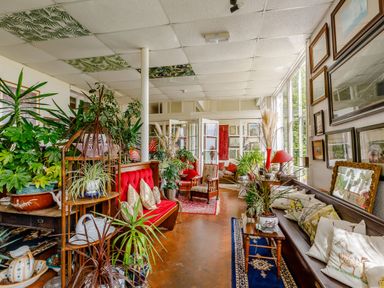 A sunroom filled with plants wooden benches with cushions framed pictures on walls and large windows at Clooneavin Apartment 8 in Lynmouth near Lynton