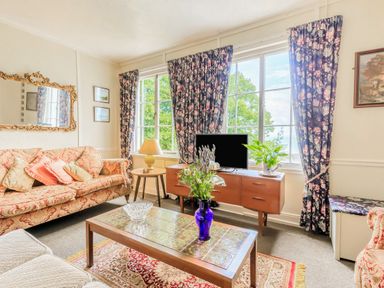 A living room with patterned sofas a wooden coffee table with flowers a TV on a wooden cabinet and floral curtains at Clooneavin Apartment 8 Lynmouth near Lynton