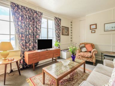 A living room with floral curtains wooden cabinet and patterned armchair at Clooneavin Apartment 8 in Lynmouth near Lynton