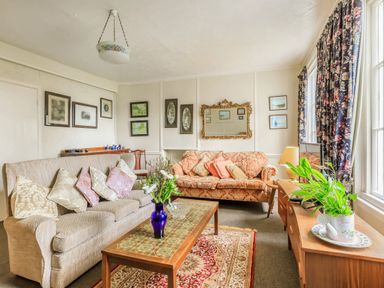 A living room with sofas a coffee table with a vase of flowers a sideboard with a plant and a lamp and framed pictures on the wall at Clooneavin Apartment 8 in Lynmouth near Lynton