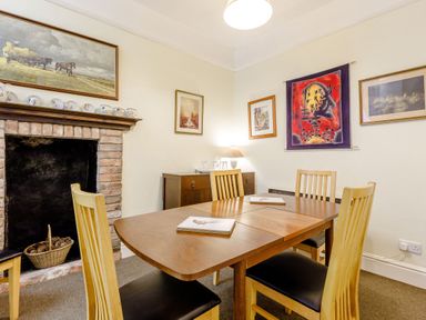 A dining room with a wooden table and four chairs near a fireplace and decorated walls at Clooneavin Apartment 8 in Lynmouth near Lynton