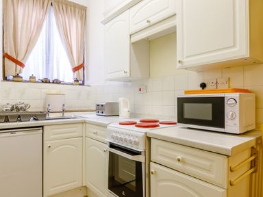 A kitchen with white cabinets electric stove microwave toaster and window with curtains at Clooneavin Apartment 8 in Lynmouth near Lynton