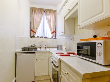 A small kitchen with white cabinets a microwave a stove sink and a window with curtains at Clooneavin Apartment 8 in Lynmouth near Lynton