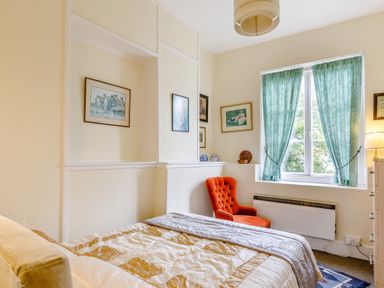 A bedroom with a bed orange armchair framed pictures on the wall and green curtains at Clooneavin Apartment 8 Lynmouth near Lynton