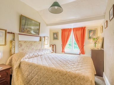A bedroom with a large bed orange curtains and framed paintings at Clooneavin Apartment 8 Lynmouth near Lynton