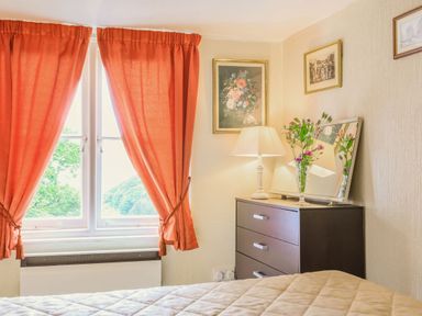 A bedroom with orange curtains a window a chest of drawers lamp mirror and flowers at Clooneavin Apartment 8 Lynmouth near Lynton