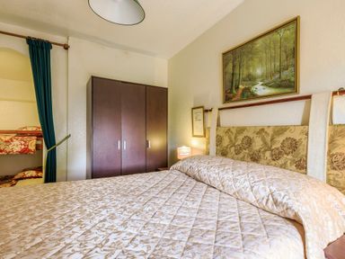A bedroom with a bed covered in a patterned quilt a dark wardrobe a lamp paintings on the wall and a bunk bed behind a green curtain at Clooneavin Apartment 8 Lynmouth near Lynton