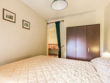A bedroom with a bed covered with a patterned quilt a dark wooden wardrobe two small paintings on the wall and an open doorway with a green curtain at Clooneavin Apartment 8 Lynmouth near Lynton