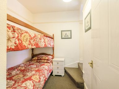 A small bedroom with bunk beds a white nightstand and carpeted stairs at Clooneavin Apartment 8 in Lynmouth near Lynton