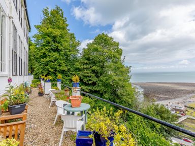 A balcony with potted plants and outdoor furniture overlooking trees and a beach at Clooneavin Apartment 8 in Lynmouth near Lynton
