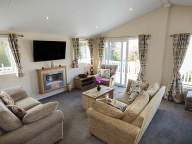 A living room with sofas a coffee table a wall-mounted television and sliding glass doors at Clearview Lodge in Borth