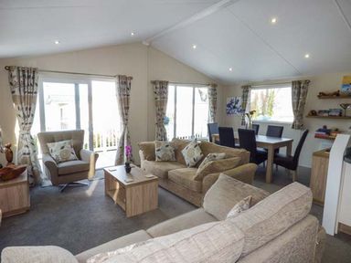 A living room with sofas armchair coffee table dining table with chairs and windows with curtains at Clearview Lodge in Borth