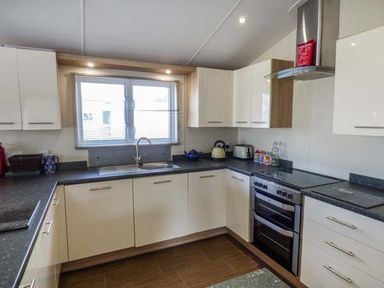 A kitchen with white cabinets black countertops a window stove kettle and toaster at Clearview Lodge in Borth