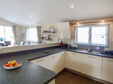A kitchen with white cabinets black countertops a bowl of fruit and dining area visible through a half wall at Clearview Lodge in Borth