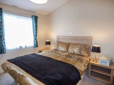 A bedroom with a double bed with gold bedding and two bedside tables with lamps at Clearview Lodge in Borth