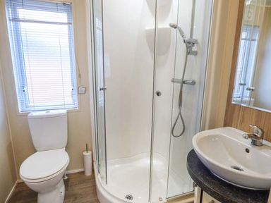 A bathroom with a toilet next to a window a glass shower enclosure and a sink with a mirror at Clearview Lodge in Borth