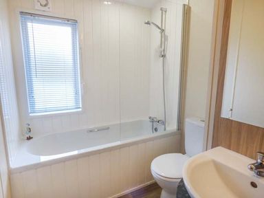 A bathroom with a bathtub with showerhead a toilet a sink and a window with blinds at Clearview Lodge in Borth
