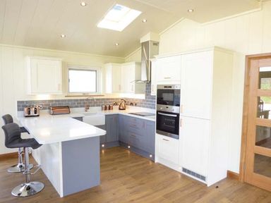 A kitchen with white and blue cabinets bar stools and wooden floor at Squirrel Lodge in Gargrave near Skipton