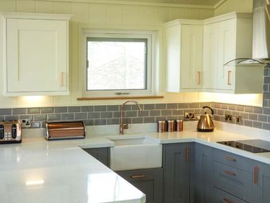 A kitchen with white and gray cabinets a window above the sink and copper appliances at Squirrel Lodge in Gargrave near Skipton