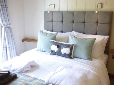 A bedroom with a bed with blue pillows and a sheep cushion at Squirrel Lodge in Gargrave near Skipton