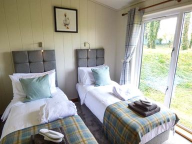 A bedroom with two single beds and towels near a window with curtains at Squirrel Lodge in Gargrave near Skipton