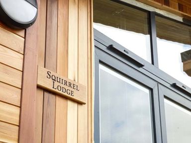 A wooden wall with a sign reading Squirrel Lodge next to a large glass window at Squirrel Lodge in Gargrave near Skipton