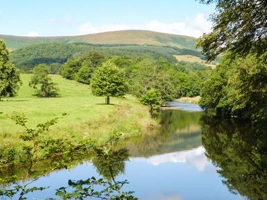 A river flowing through green fields and trees with hills in the background at Squirrel Lodge in Gargrave near Skipton