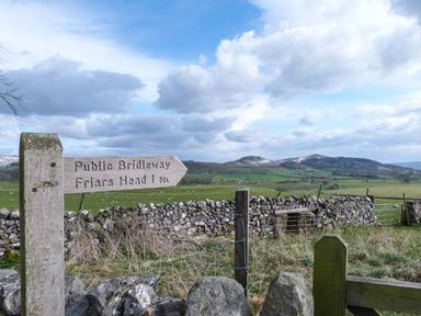 A wooden signpost indicating public bridleway directions with a stone wall and hills in the background at Squirrel Lodge in Gargrave near Skipton