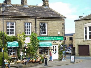 A stone building with green awnings and baskets outside showing The Dalesman Cafe Tea Rooms in Gargrave near Skipton