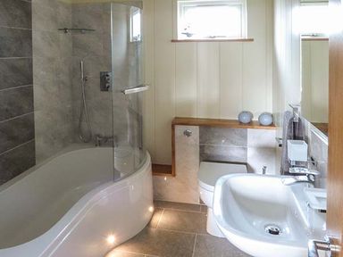 A bathroom with a curved bathtub shower enclosure a toilet and a sink at Squirrel Lodge in Gargrave near Skipton