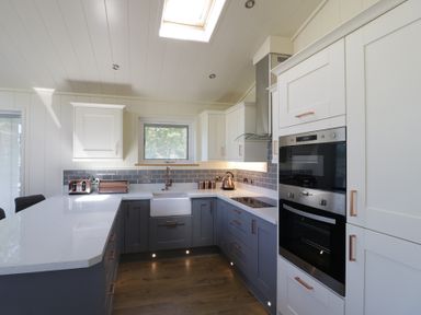 A kitchen with white and grey cabinetry a built-in oven a sink a countertop and a window at Squirrel Lodge in Gargrave near Skipton