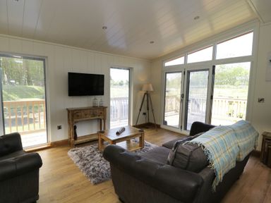 A sitting room with sofas a wooden coffee table a rug a wall mounted television and large windows at Squirrel Lodge in Gargrave near Skipton