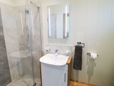A bathroom with a shower enclosure a sink with cabinet a mirror a towel and toilet paper holder at Squirrel Lodge in Gargrave near Skipton