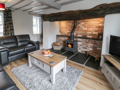 A living room with a wood stove fireplace leather sofas wooden coffee table and a television at Bryndan in Machynlleth