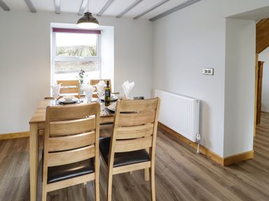 A dining area with a wooden table set with plates, glasses, cutlery, and napkins near a window at Bryndan in Machynlleth