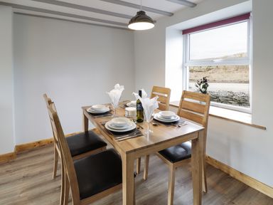 A dining room with a wooden table set for four near a window with a vase of flowers at Bryndan in Machynlleth