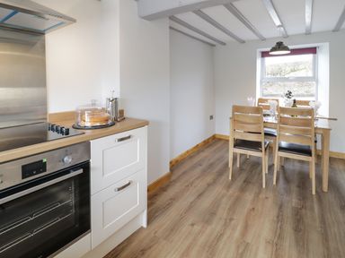 A kitchen with an oven and cooktop and a dining table with four chairs near a window at Bryndan in Machynlleth