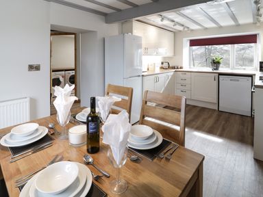 A kitchen with white cabinets a dining table set for four and a view into a laundry room at Bryndan in Machynlleth