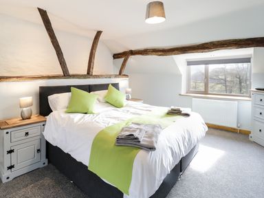 A bedroom with a bed with green pillows and runner bedside tables lamps a window and wooden beams at Bryndan in Machynlleth